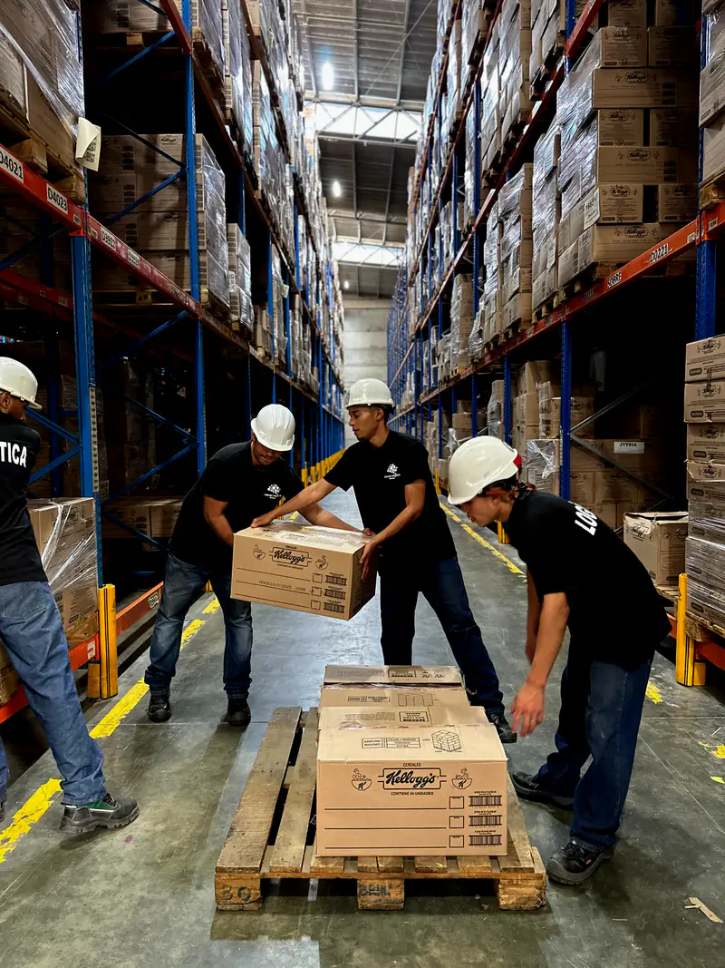 Equipo de Deluxe Logistics con casco revisando y movilizando cajas sobre una estiba en una bodega de estanterías altas